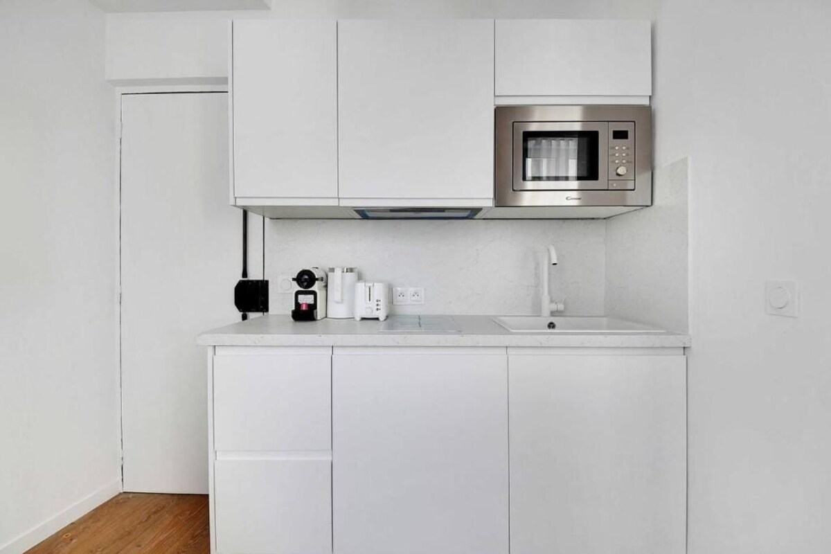 Una cocina compacta con muebles blancos, un microondas de acero inoxidable, una cafetera y un tostador.
