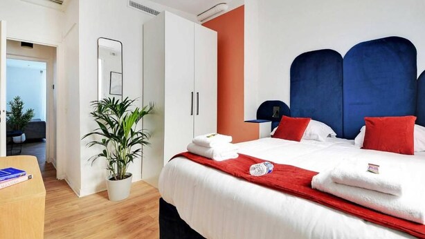 Une chambre d’hôtel avec un lit, une plante en pot, un bureau et une armoire.