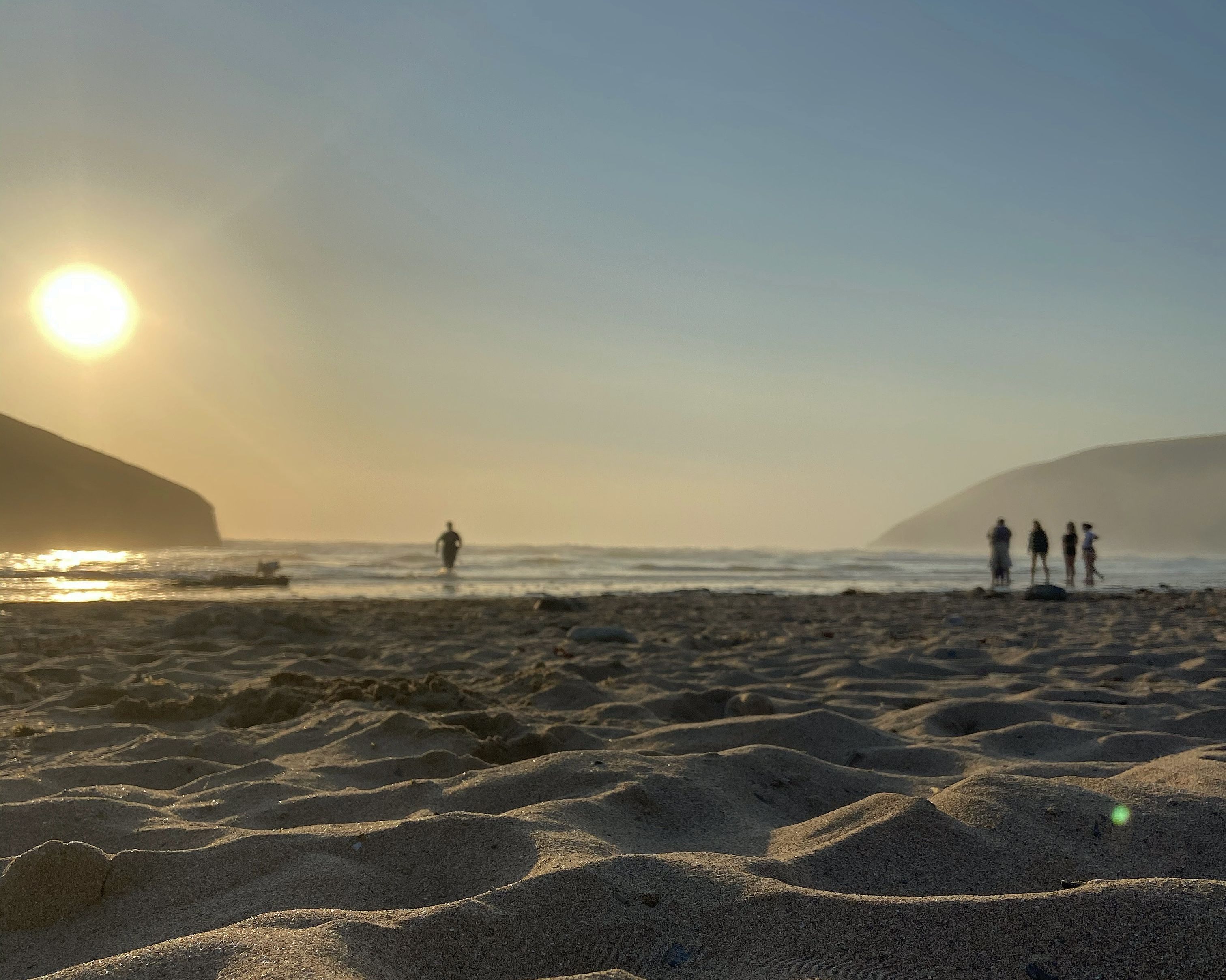 Ein Strand mit Dünen und einem Sonnenuntergang im Hintergrund.