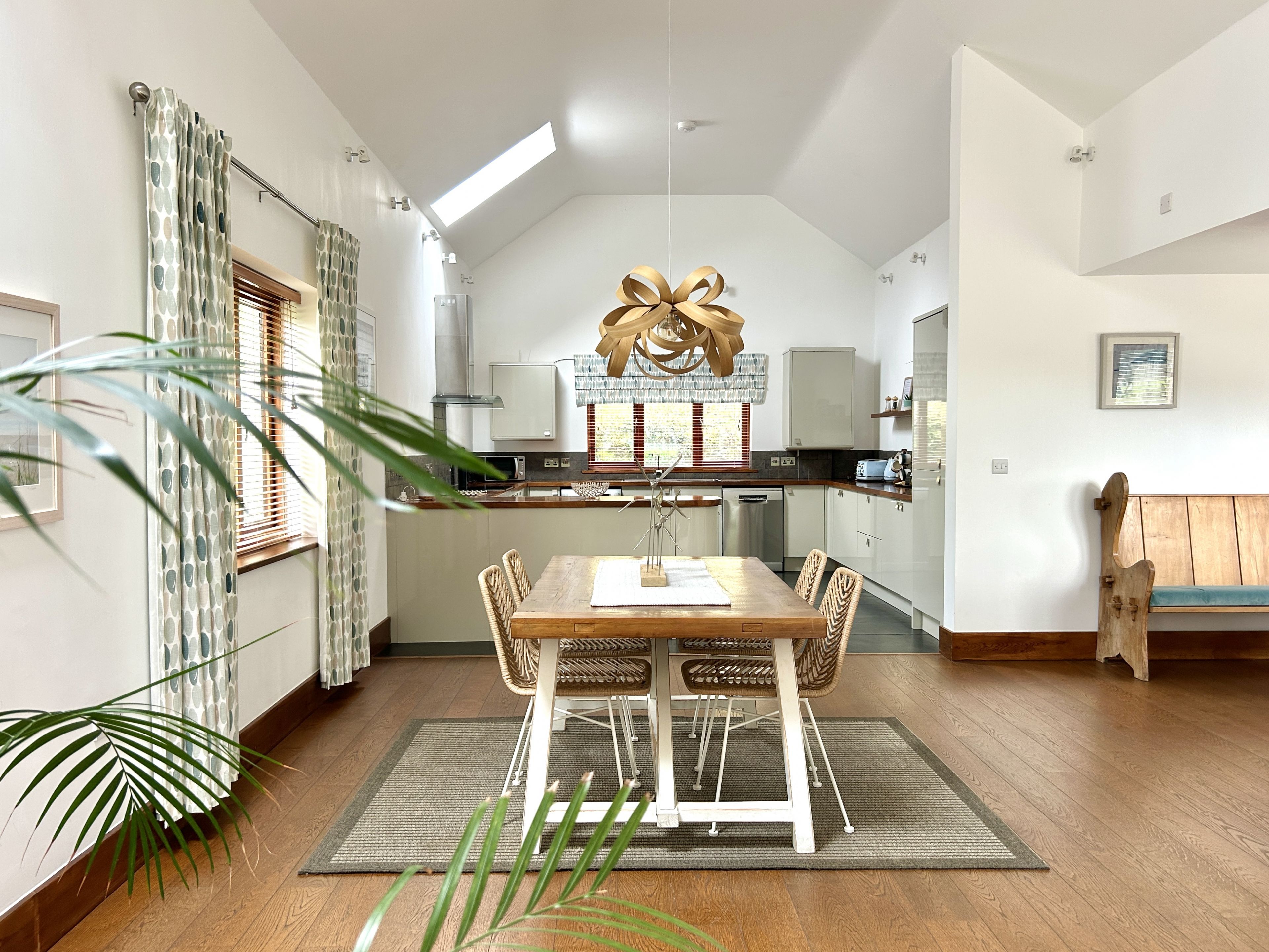 Una cocina moderna con armarios blancos, una mesa de comedor de madera y una lámpara de techo original.