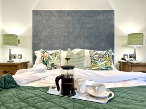 Una cama bien hecha con un edredón verde, una cafetera, dos tazas y una bandeja con un mapa.