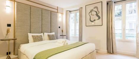 Une chambre moderne avec un grand lit, des tables de chevet, une œuvre d’art accrochée au mur et une vue par la fenêtre.