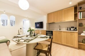 A modern kitchen with wooden cabinets, a dining area with a round table, and a flat-screen TV mounted above the counter. - Opéra - Elégant appartement - Haystia (Paris)