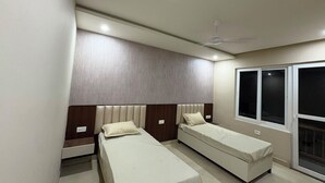 Une chambre avec deux lits simples, un ventilateur de plafond et une fenêtre avec des stores.