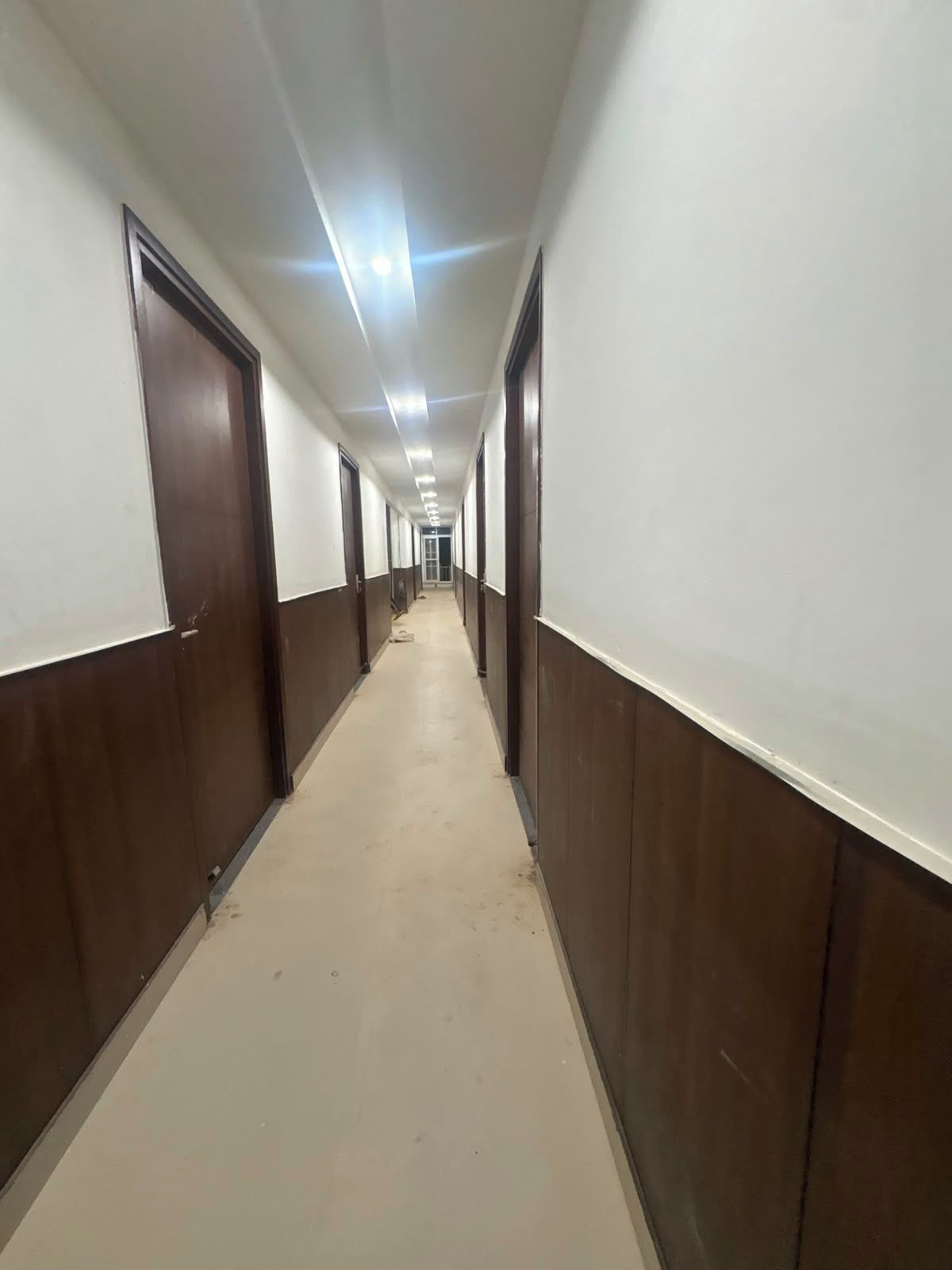 Un long couloir étroit, avec des portes de part et d’autre, qui mène à une porte au bout.