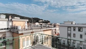Um edifício residencial com vários andares, varandas, vista para o mar e paisagem montanhosa ao fundo.