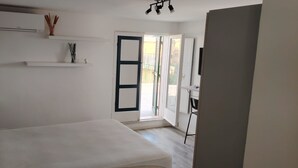 Quarto com cama, escrivaninha e porta que dá para uma área externa.