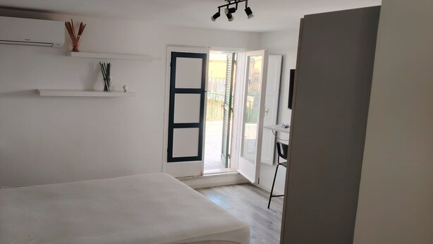 Una habitación con cama, escritorio y puerta que da a un espacio exterior.