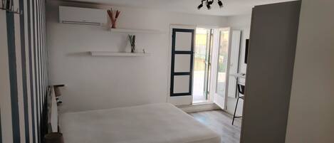 A room with a bed, a desk, and a door leading to an outdoor area.