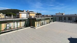 Un espacio exterior amplio con piso empedrado, cerca metálica verde y edificios al fondo.
