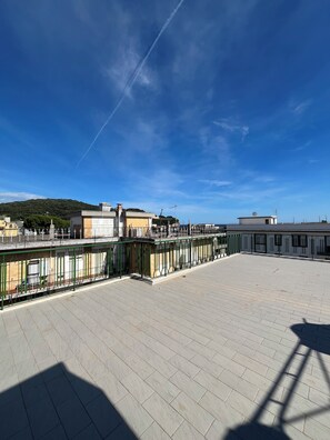A spacious outdoor area with a paved floor, a green metal fence, and buildings in the background. - Terrazza sul Mare (Gaeta)