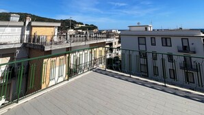 Terraço no telhado com céu claro, edifícios ao fundo e vista distante do mar.
