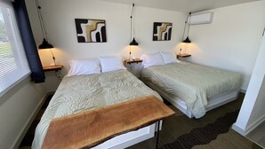 Ein Zimmer mit zwei Betten, einer Holzbank, Wandbildern und einer Deckenleuchte.