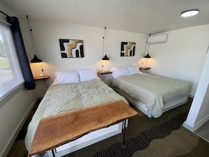 Ein Zimmer mit zwei Betten, einer Holzbank, Wandbildern und einer Deckenleuchte.