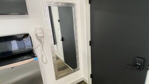Ein Hotelzimmer mit einer Mikrowelle, einem Telefon, einem Spiegel mit dekorativem Rahmen und einer dunklen Tür.