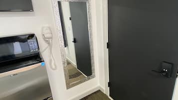 Ett hotellrum med en mikrovågsugn, en telefon, en spegel med en dekorativ ram och en mörk dörr.
