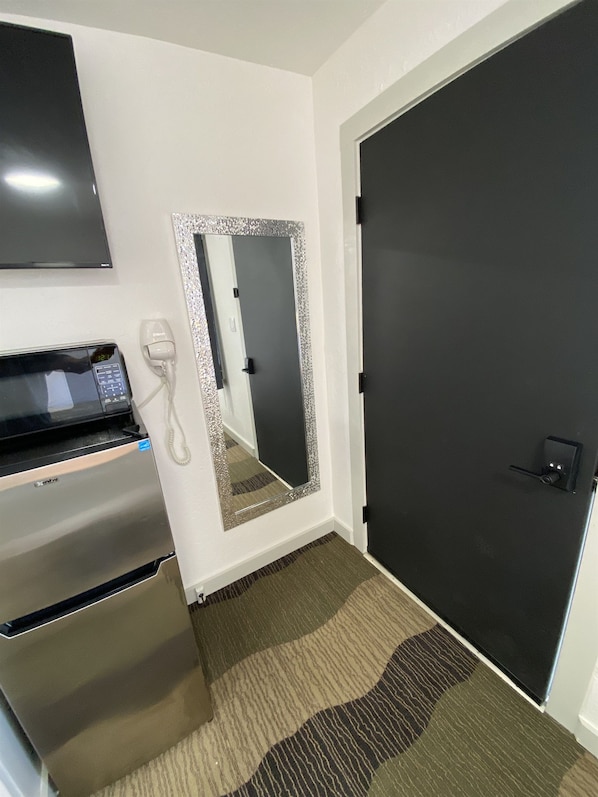 A hotel room with a microwave, a telephone, a mirror with a decorative frame, and a dark door.