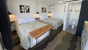 Ein Hotelzimmer mit zwei Betten, einem Holztisch, einem Badezimmer mit Toilette und einer Duschkabine.