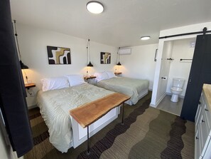 Ein Hotelzimmer mit zwei Betten, einem Holztisch, einem Badezimmer mit Toilette und einer Duschkabine.