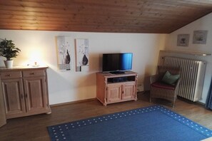 A room with a wooden ceiling, a television on a wooden cabinet, a potted plant, and a blue rug. - Holiday apartment with 1 bedroom (Bernau am Chiemsee)