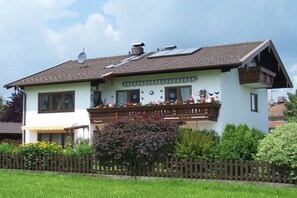 A two-story house with a balcony, a satellite dish, and a garden with flowers. - Holiday apartment with 1 bedroom (Bernau am Chiemsee)