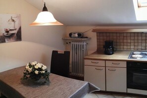 A compact kitchen with a dining table, a radiator, a coffee maker, and a stove. - Holiday apartment with 1 bedroom (Bernau am Chiemsee)