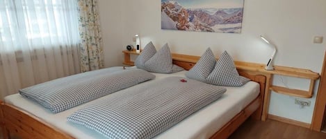 Una cama doble con ropa de cama a cuadros, una mesita de noche con lámpara, un cuadro en la pared y una ventana con cortinas.