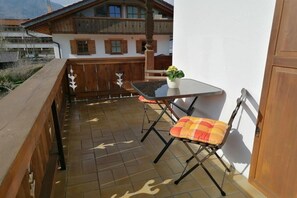 Ein Balkon mit Holzgeländer, einem Tisch, zwei Stühlen und einem Blumentopf.