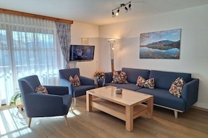 Ein Wohnzimmer mit einer Sofagarnitur, einem Couchtisch, einem Fernseher und einem Bild an der Wand.