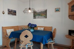 A dining area with a wooden bench seating arrangement, a table with a blue tablecloth, and a hanging light fixture. - Anna holiday apartment (Garmisch-Partenkirchen)