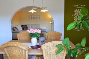 A dining area with wicker chairs, a wooden table, a vase with flowers, and a wall with a heart-shaped design. - Holiday apartment with 3 bedrooms (Zwiesel)