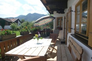 Eine Holzterrasse mit Tisch und Stühlen, einem gestreiften Sonnenschirm und Blick auf die Berge.