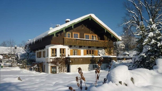 Un bâtiment de style chalet, doté d’un toit en pente, d’un balcon en bois et entouré d’un paysage enneigé.