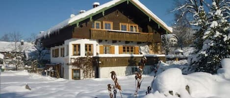 Un bâtiment de style chalet, doté d’un toit en pente, d’un balcon en bois et entouré d’un paysage enneigé.