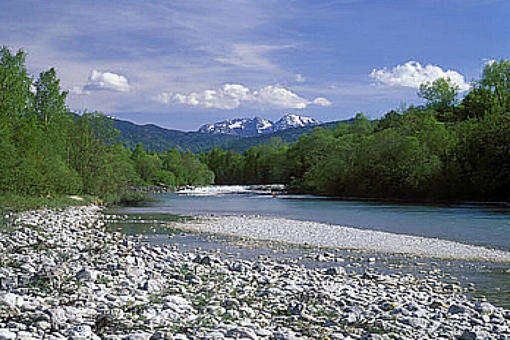 Une rivière au lit rocheux, bordée d’une végétation luxuriante et avec des montagnes en arrière-plan.