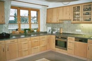 A kitchen with wooden cabinets, a window with curtains, a coffee maker, and a stove. - Holiday apartment with 2 bedrooms (Lenggries)