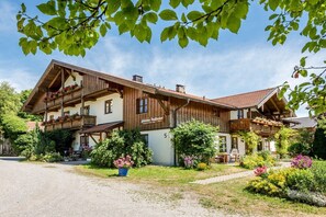 En tvåvånings chalet i trä med balkonger, omgiven av frodig grönska och blommor.
