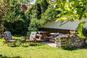 An outdoor seating area with chairs and tables, surrounded by greenery and a stack of firewood. - At Paulfischer right on Lake Chiemsee (Chieming)