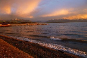 A waterfront view with a pier extending into calm waters, a mountain range in the background, and a clear sky. - At Paulfischer right on Lake Chiemsee (Chieming)