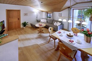 A cozy living room with a sofa, dining table, and a TV. - At Paulfischer right on Lake Chiemsee (Chieming)