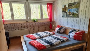 Ein Zimmer mit einem Bett, einem Vorhangfenster, einem Heizkörper und einer Wand mit einer strukturierten Oberfläche.