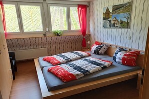 A room with a bed, a window with curtains, a radiator, and a wall with a textured pattern. - Holiday apartment with 2 bedrooms (Graach)