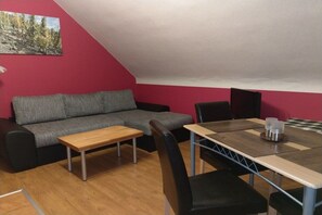Una habitació amb un sofà gris, una taula de centre de fusta, una taula de menjador amb cadires i una paret vermella d'accentuació.