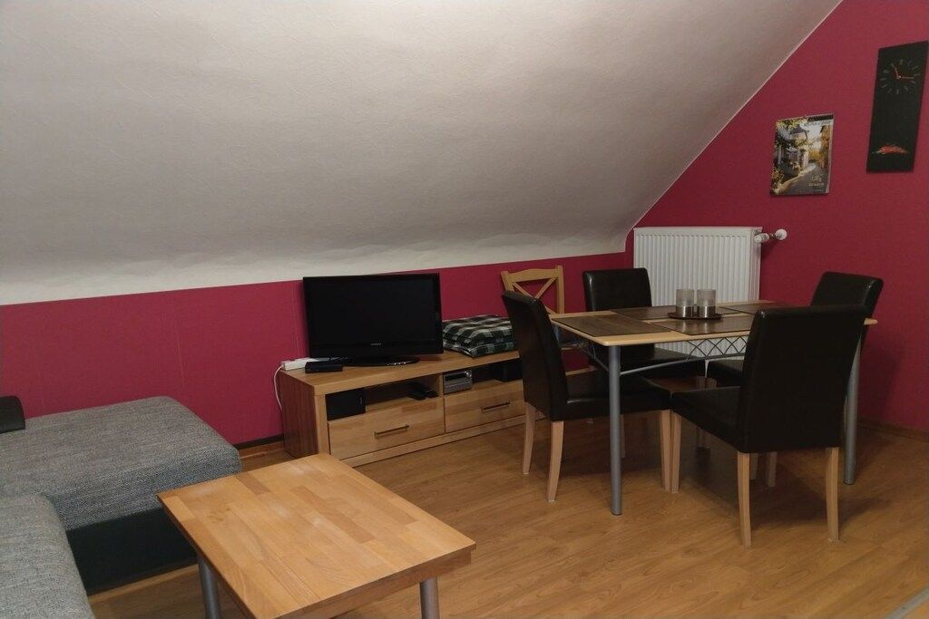 Een kamer met een eettafel, stoelen, een televisie en een bank.