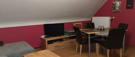 A room with a dining table, chairs, a television, and a sofa.