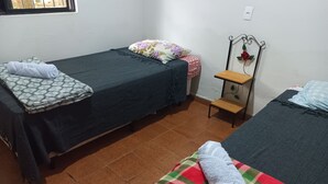 Una habitación con dos camas individuales, una mesita de madera, un estante en la pared y una ventana con vistas.