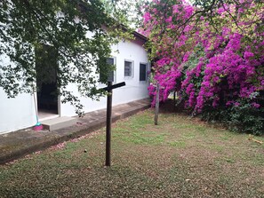 Edifício branco com entrada pavimentada e uma árvore com flores cor-de-rosa.