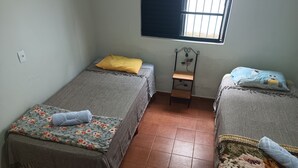 Una habitación pequeña y limpia con dos camas individuales, una mesita y una ventana con barrotes.