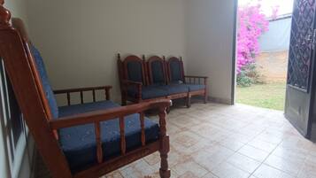 A room with two wooden chairs and a bench, a tiled floor, and a view of a garden through an open door.