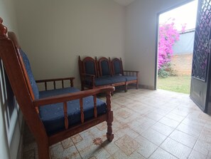 A room with two wooden chairs and a bench, a tiled floor, and a view of a garden through an open door.